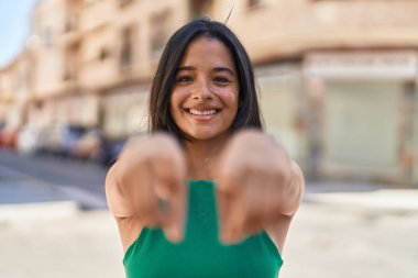 Young hispanic woman smiling confident pointing with fingers at street