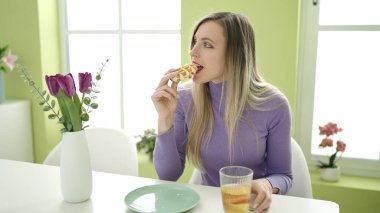 Genç sarışın kadın kahvaltı yapıyor. Evde masada oturuyor.