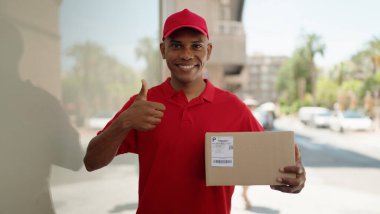 Young latin man delivery worker holding package doig ok gesture with finger at street