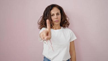 Orta yaşlı İspanyol kadın, izole edilmiş pembe arka planda parmağıyla hayır diyor.