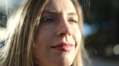 Young blonde woman looking to the side with relaxed expression at street