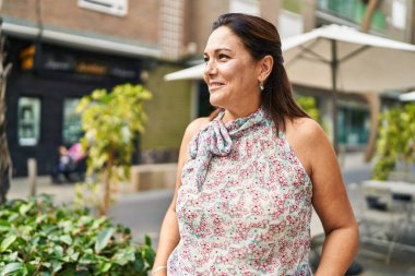 Orta yaşlı İspanyol kadın sokakta kendine güvenerek gülümsüyor.