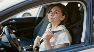 Orta yaşlı İspanyol kadın sokakta kemer takarak gülümsüyor.