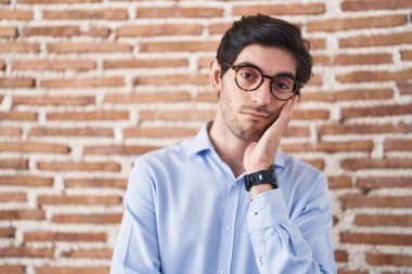 Tuğla duvar arkasında duran İspanyol genç adam kollarını kavuşturarak depresyondan sıkılmış ve yorgun göründüğünü düşünüyor.. 