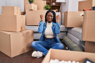 Afro-Amerikalı kadın yeni evinde kazanan ifadesiyle yerde oturuyor.