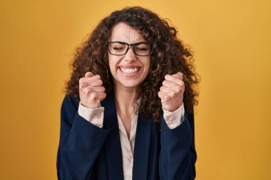 Sarı arka planda dikilen kıvırcık saçlı İspanyol kadın kollarını kaldırmış ve gözleri kapalı zaferi kutluyor. Kazanan konsept. 