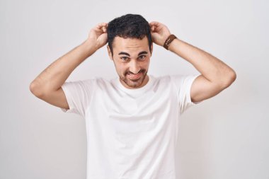Beyaz arka planda duran yakışıklı İspanyol adam komik ve deli pozu veriyor parmakları kafasında tavşan kulağı, neşeli bir gülümseme 