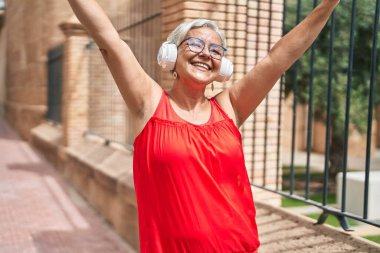 Orta yaşlı, kır saçlı, müzik dinleyip sokakta dans eden bir kadın.