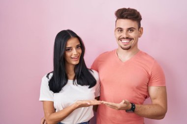 Pembe arka planda duran genç İspanyol çift avuçlarını açıp fotokopi alanını gösteriyor. 