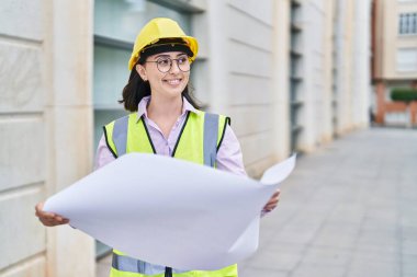 Young hispanic woman architect reading plans at street