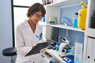 Genç, güzel İspanyol bilim kadını gülümseyen kendine güvenen yazma raporu laboratuvarda çalışıyor.