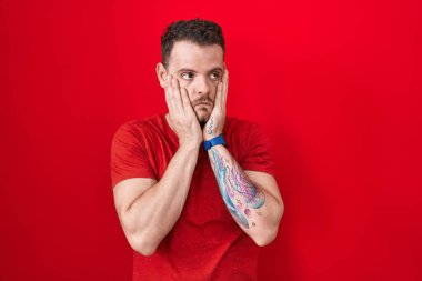 Young hispanic man standing over red background tired hands covering face, depression and sadness, upset and irritated for problem 