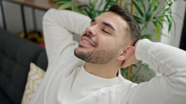 Genç İspanyol adam, ellerini başının üstüne koyup evinde kanepede oturarak rahatladı.