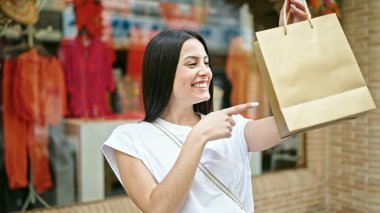 Genç ve güzel İspanyol kadın gülümsüyor alışverişe gidiyor giyim mağazasını işaret ediyor.