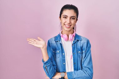 Pembe arka planda duran genç ve güzel bir kadın neşeli bir şekilde sunum yapıyor ve avuç içi kameraya bakıyor.. 