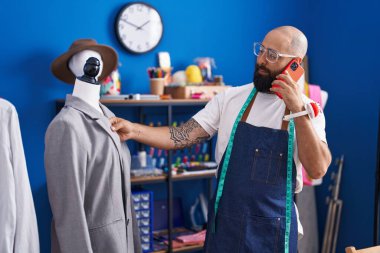 Genç kel bir terzi elbise fabrikasında akıllı telefondan konuşuyor.