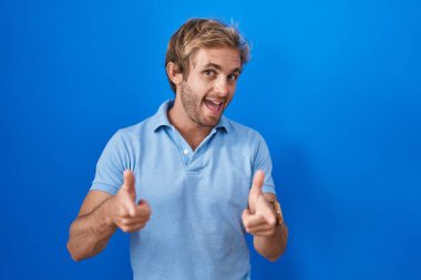 Mavi arka planda dikilen beyaz adam mutlu ve komik yüzüyle kamerayı işaret ediyor. iyi enerji ve titreşimler. 