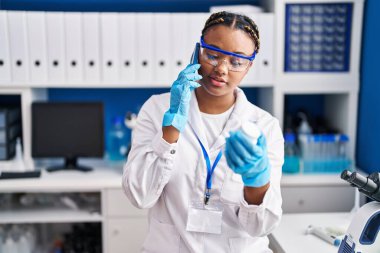 Afrika kökenli Amerikalı bilim kadını laboratuvarda elinde haplarla akıllı telefondan konuşuyor.