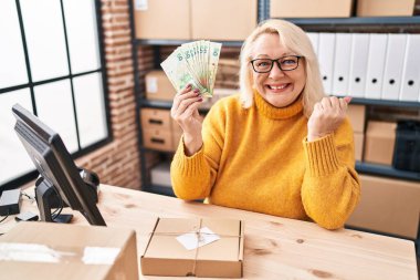 Orta yaşlı beyaz bir kadın küçük işletme şirketinde çalışıyor elinde Hong Kong dolarları tutarak gururla haykırıyor zaferi ve başarıyı kutluyor. 