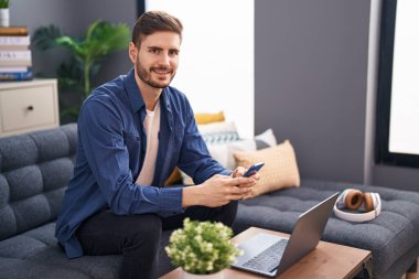 Young caucasian man using smartphone and laptop at home