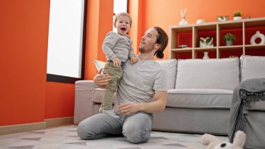 Baba ve oğul yerde oturup birbirlerine sarılıyorlar.