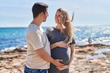 Erkek ve kadın bir arada, deniz kenarında göbeğe dokunuyorlar.