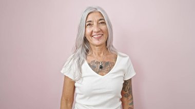 Orta yaşlı, gri saçlı, gülümseyen, kendine güvenen, soyutlanmış pembe arka planda duran kadın.