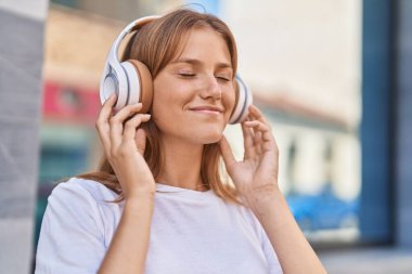 Young blonde girl smiling confident listening to music at street