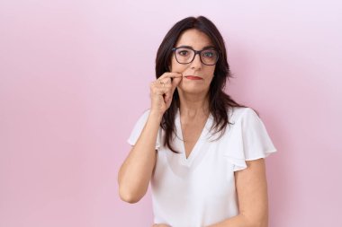 Orta yaşlı İspanyol kadın, günlük beyaz tişört ve gözlük takıyor ağzı ve dudakları parmaklarıyla fermuar gibi kapalı. gizli ve sessiz, tabu konuşması 