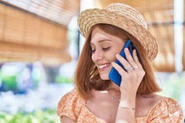 Genç, kızıl saçlı, yaz şapkalı bir turist sokakta akıllı telefondan konuşuyor.