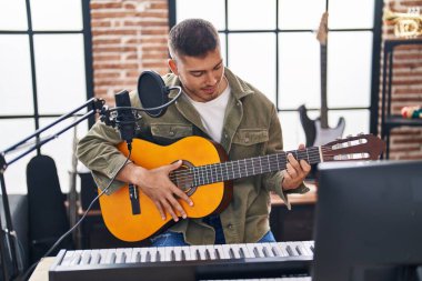 Young hispanic man musician singing song playing classical guitar at music studio