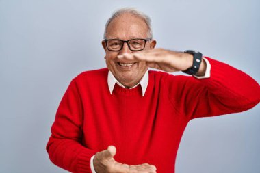 İzole edilmiş arka planda gri saçlı yaşlı bir adam. Elleri büyük ve büyük boy işareti, ölçü sembolü gösteriyor. Kameraya bakıp gülümsüyor. ölçüm kavramı. 