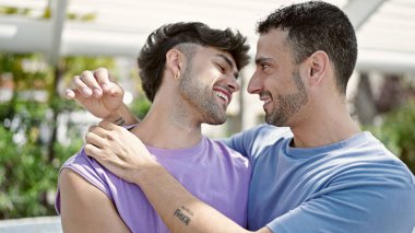 Two men couple smiling confident hugging each other at park