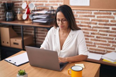 Ofiste çalışan genç İspanyol iş kadını laptopu kullanıyor.