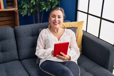 Middle age woman using touchpad sitting on sofa at home