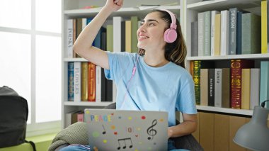 Young beautiful hispanic woman student listening to music dancing at library university