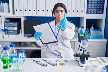 Hispanic young woman working at scientist laboratory showing middle finger, impolite and rude fuck off expression 