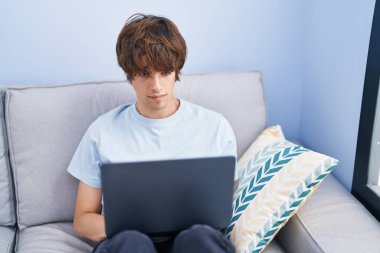 Evdeki masada dizüstü bilgisayar kullanan genç sarışın adam.