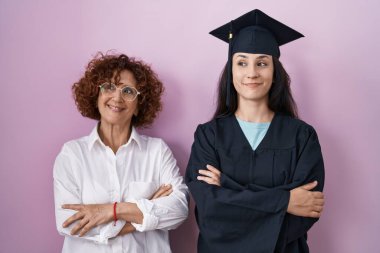 Latin kökenli anne ve kız mezuniyet şapkası ve tören cübbesi takıyor gülümsüyor ve yan tarafa bakıyor ve düşünüyor.. 