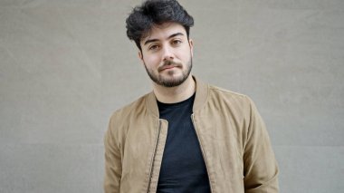 Young hispanic man standing with serious expression over isolated white background
