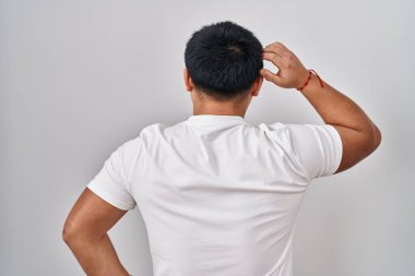 Genç Çinli adam beyaz arka planda geriye doğru duruyor. Elleri başının üstünde şüpheyi düşünüyor. 