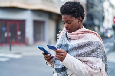 African american woman using smartphone and credit card at street