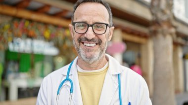 Orta yaşlı doktor sokakta kendine güvenen gülümsüyor.