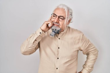 Gri saçlı, soyutlanmış arka planda duran orta yaşlı bir adam. Elleri çenesinde soru sorarken, düşünceli bir ifade takınıyor. Düşünceli bir yüzle gülümsüyor. şüphe kavramı. 