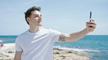 Genç İspanyol adam gülümsüyor sahildeki akıllı telefonun yanında özçekim yapıyor.