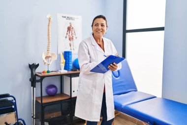 Orta yaşlı İspanyol kadın fizyoterapist rehabilitasyon kliniğinde panoya yazı yazıyor.