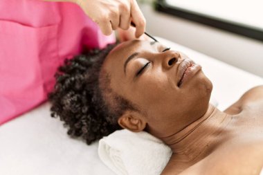 African american woman lying on massage table having eyebrows treatment at beauty salon