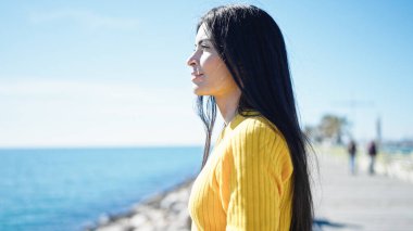 Genç ve güzel İspanyol kadın deniz kenarında rahat bir ifadeyle yan tarafa bakıyor.