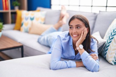 Young beautiful hispanic woman smiling confident lying on sofa at home