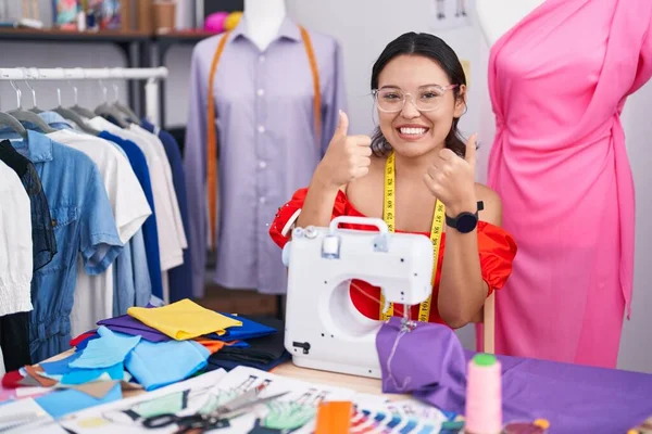 西班牙裔年轻女性服装设计师用缝纫机的成功标志做了积极的手势 竖起大拇指 笑容满面 喜形于色 快乐的表达和胜利的姿态 — 图库照片
